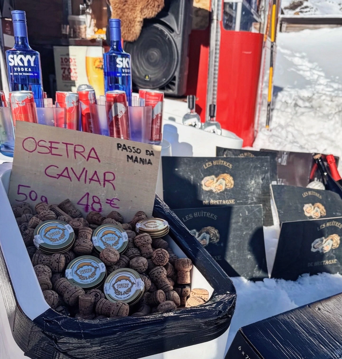 Outdoor bar in the snow with vodka, red cans, caviar, oysters and a speaker.