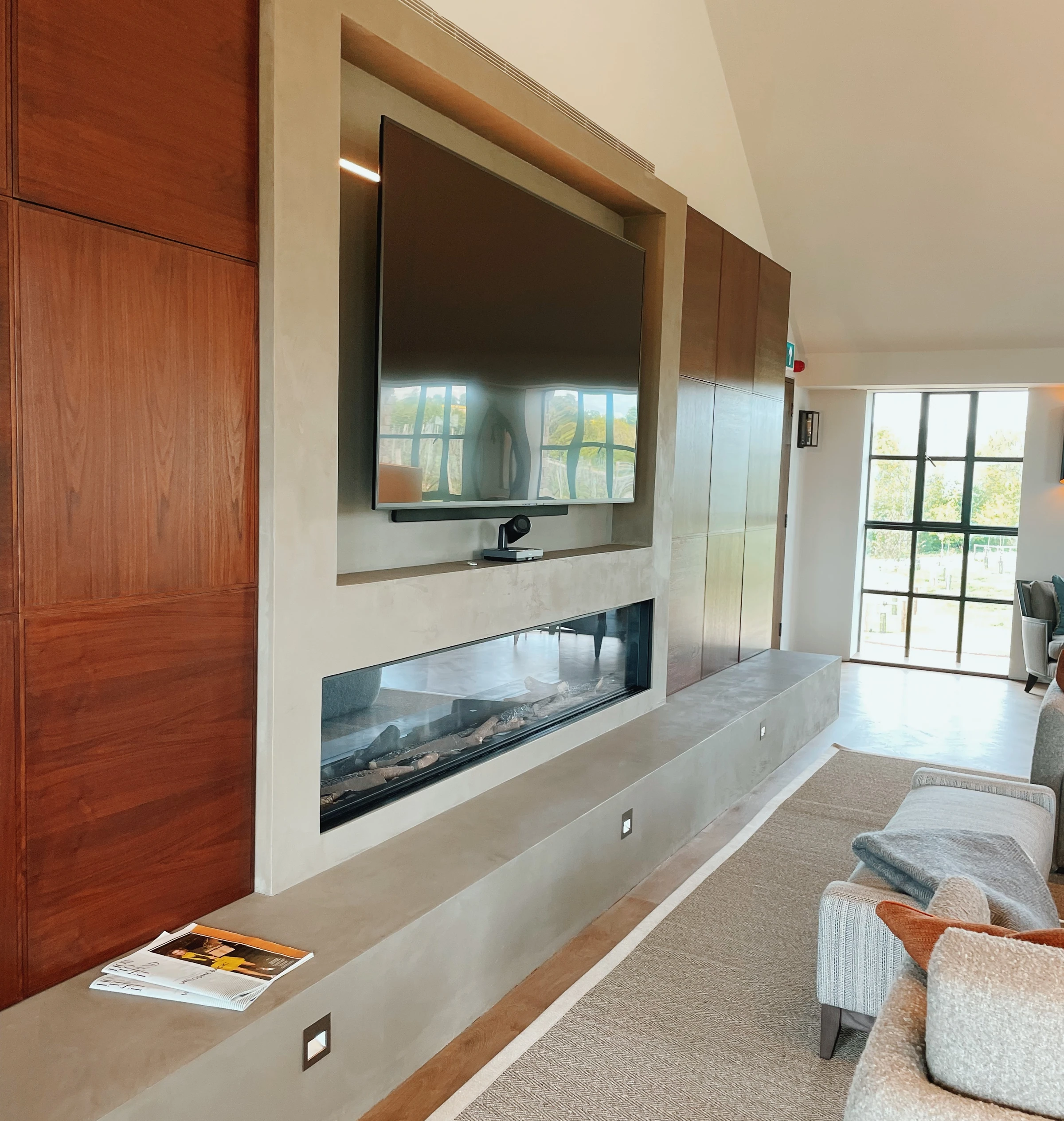 Modern tasting room with a large television above a long glass-fronted fireplace, wood panelling and sofas