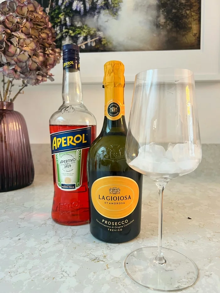 Aperol and Prosecco bottle beside empty wine glass on marble counter