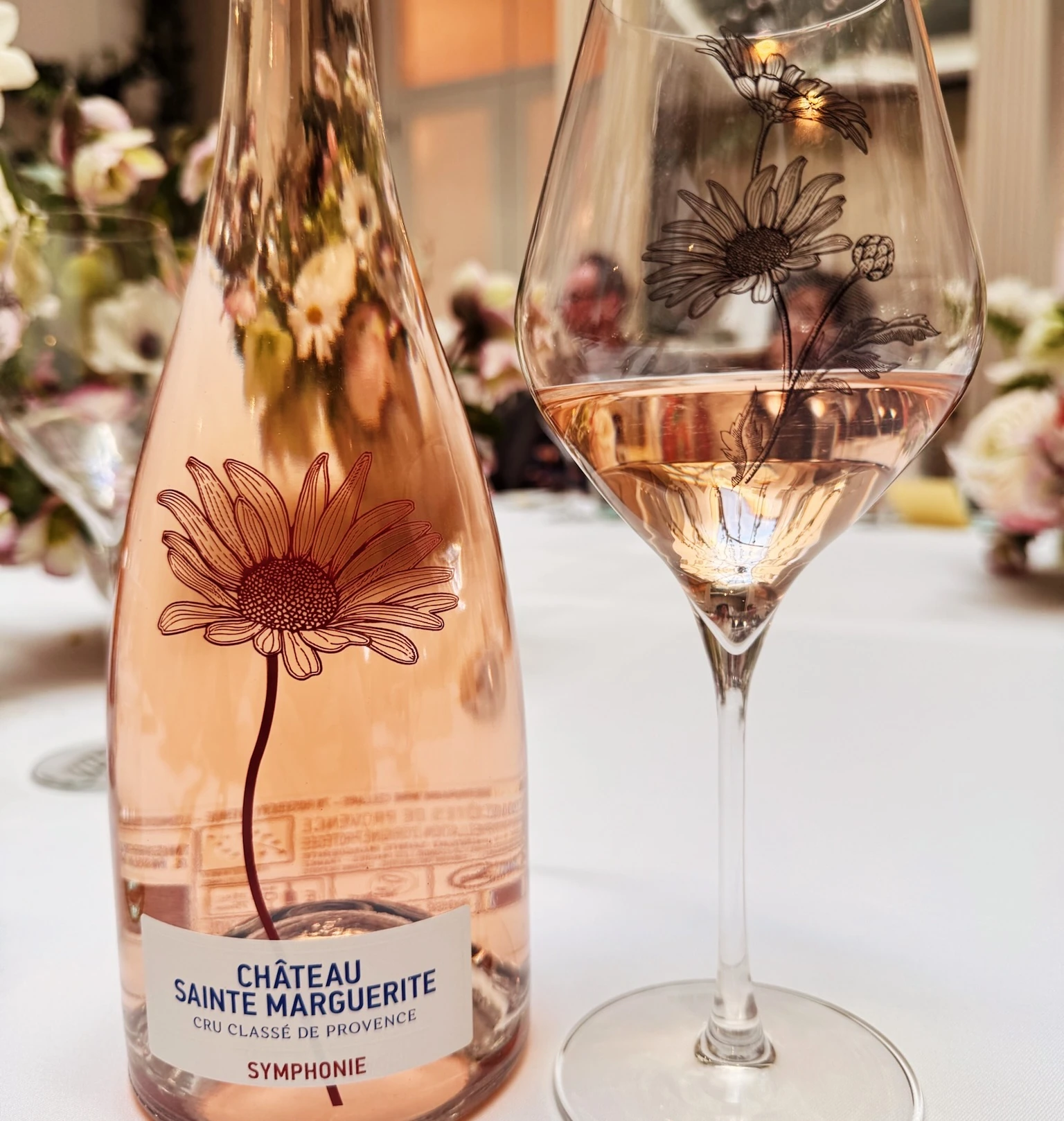 Bottle of Château Sainte Marguerite rosé beside a floral wine glass, with flowers on a table