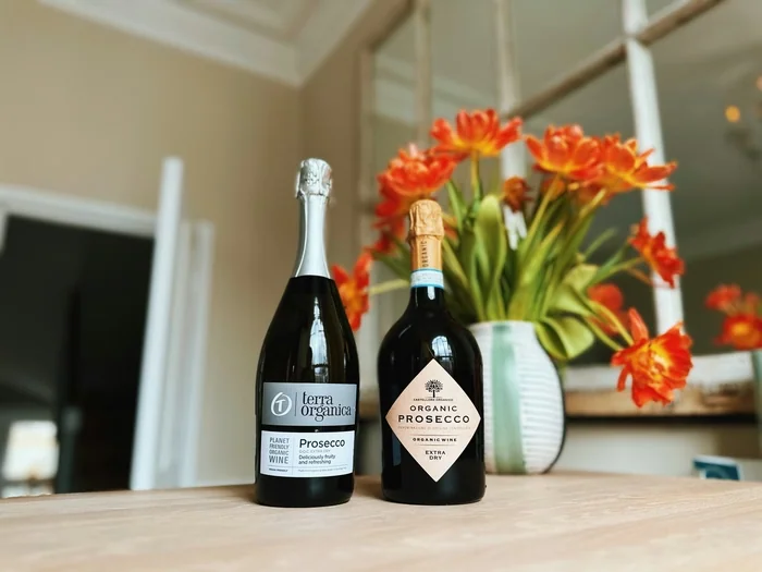 Two organic Prosecco bottles with orange flowers in vase