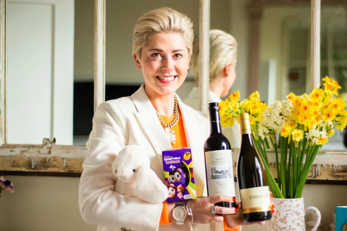Smiling woman holding wine bottles, chocolate and a white plush rabbit