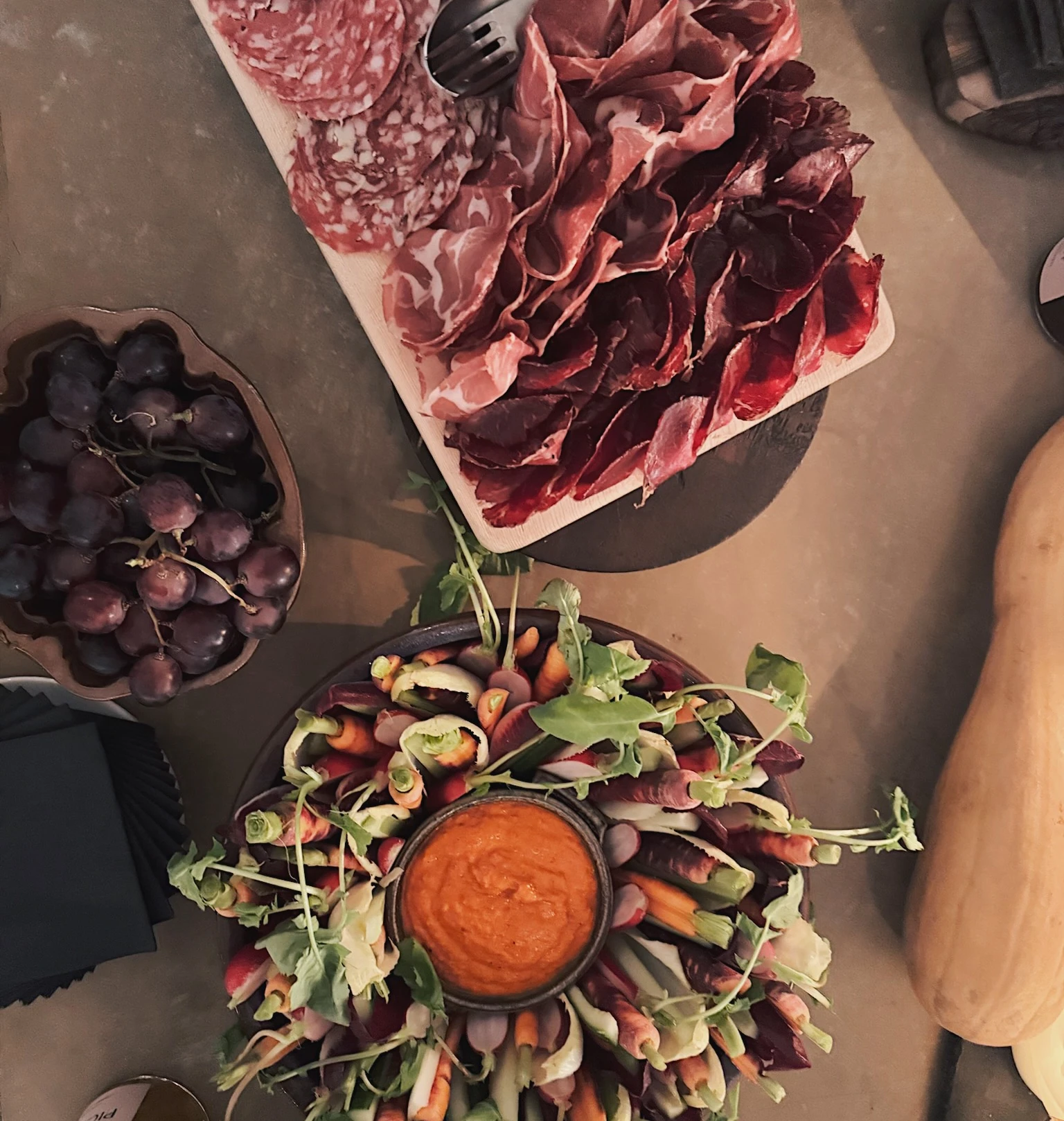 Charcuterie board, grapes and a vegetable platter with dip arranged on a table