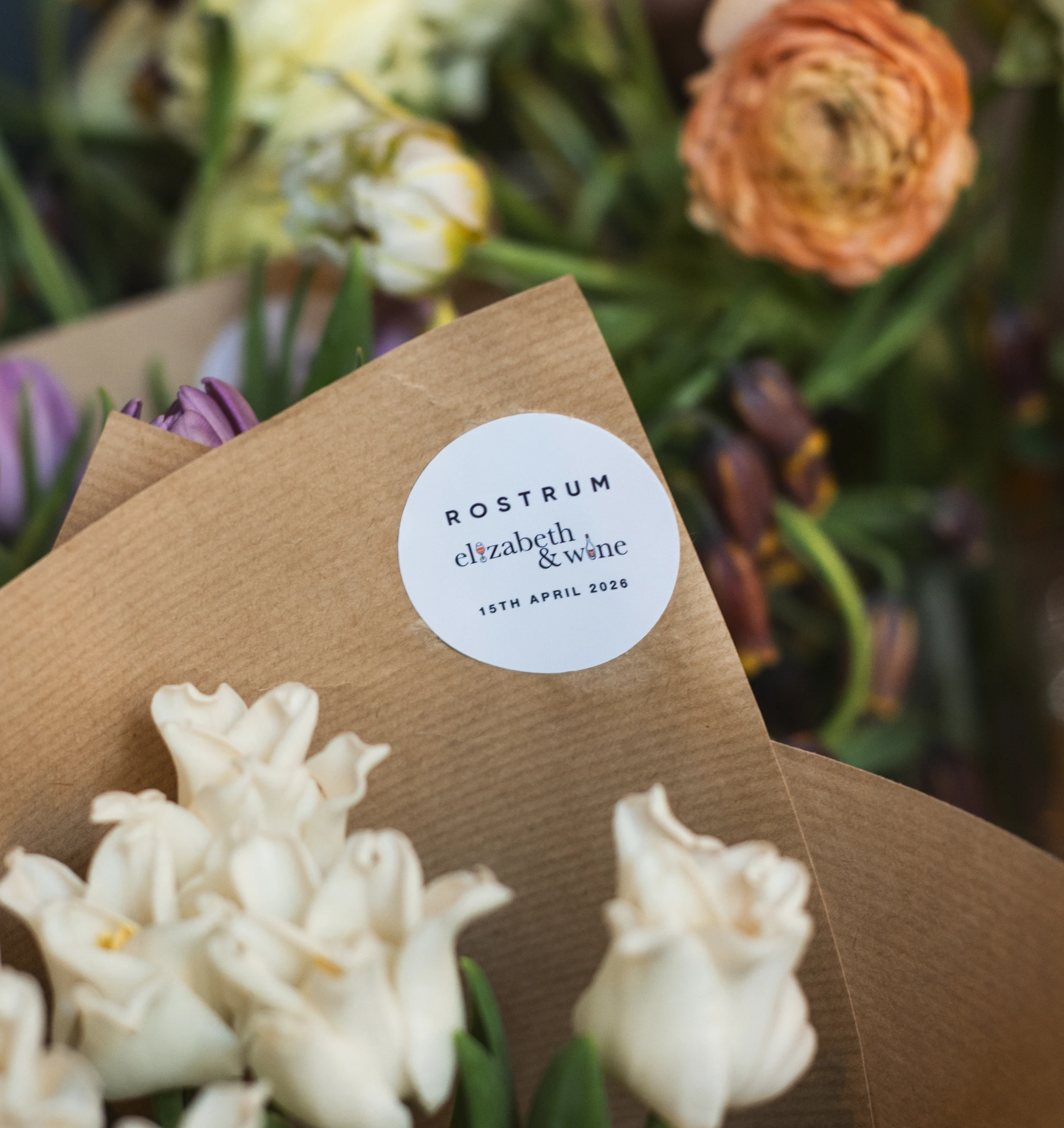 Flower arrangements with a branded Rostrum and Elizabeth & Wine event card dated 15th April 2026