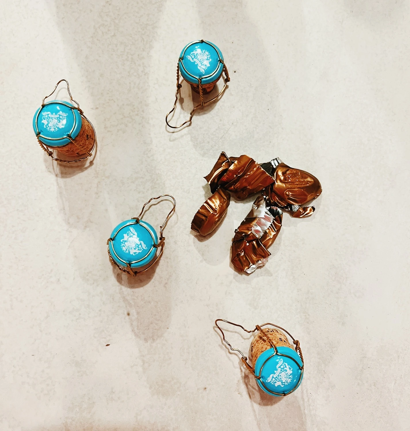 Four turquoise-topped sparkling wine corks and crumpled copper foil on a pale surface