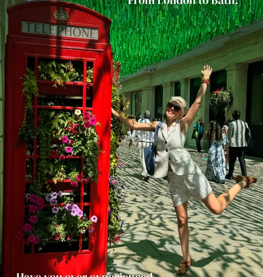 Woman posing beside a flower-filled red telephone box beneath green decorations