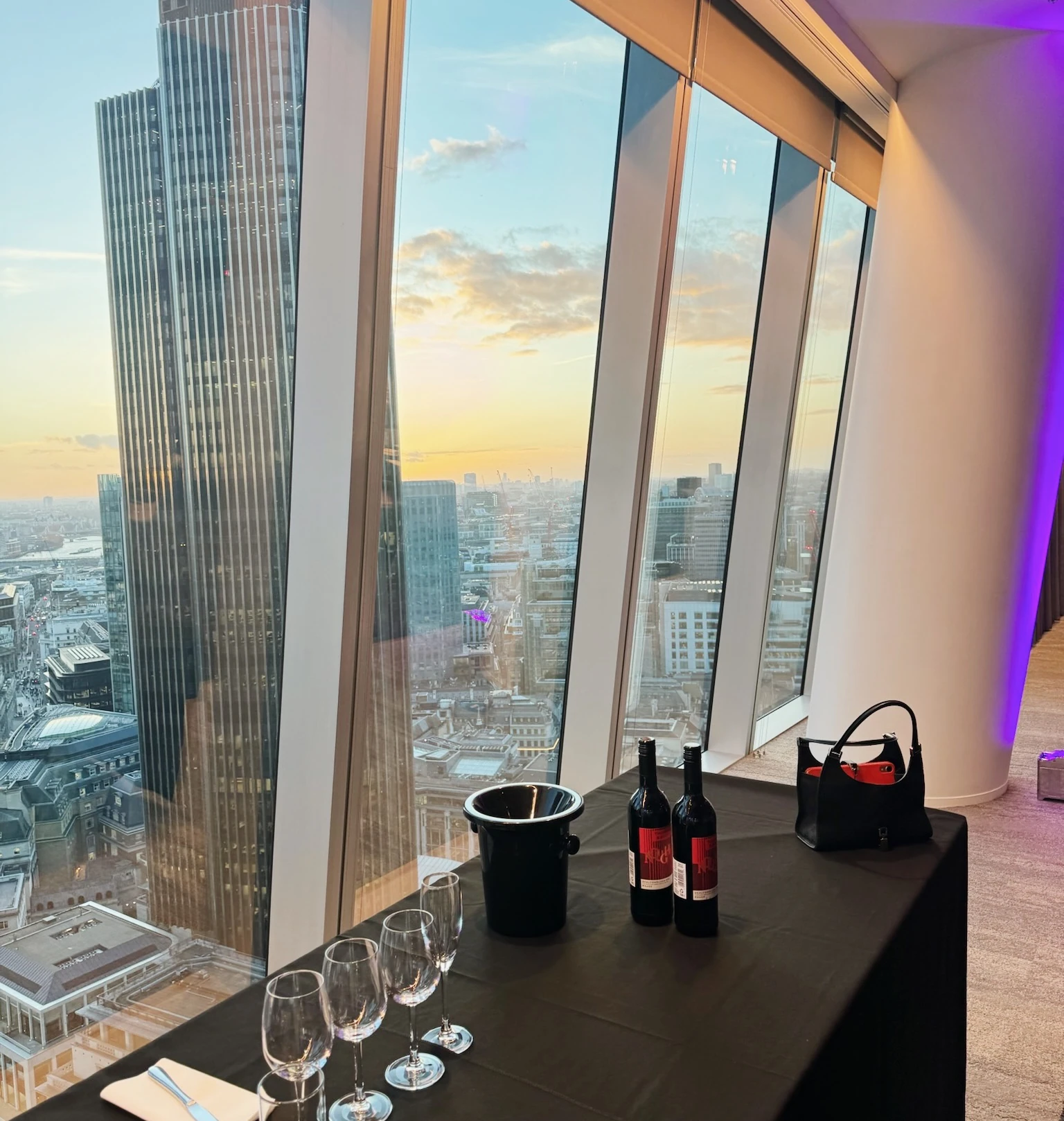 Wine tasting table beside floor-to-ceiling windows overlooking London at sunset