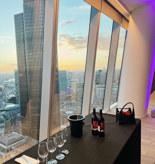Wine tasting table beside floor-to-ceiling windows overlooking London at sunset
