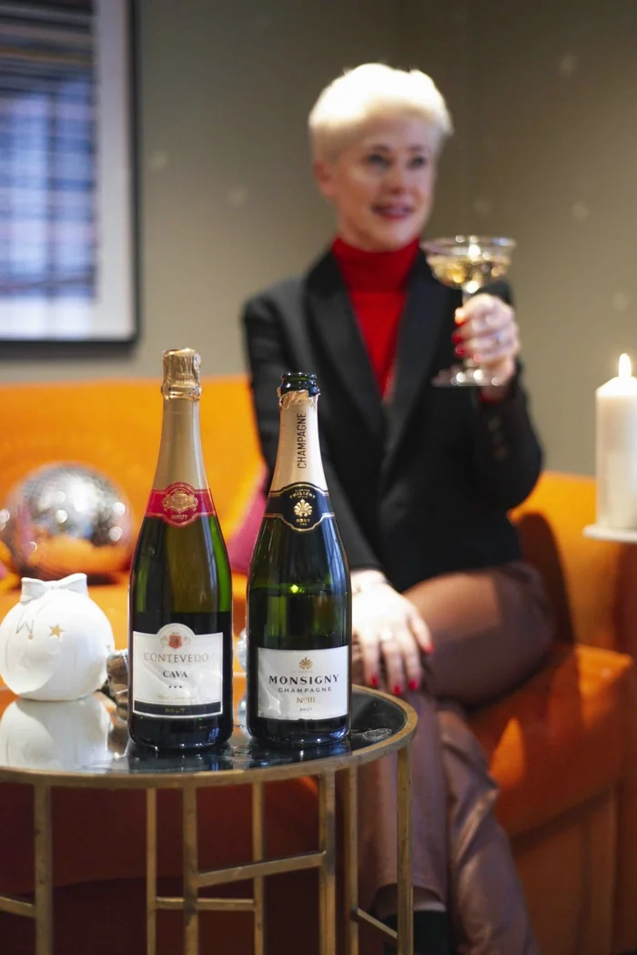 Two champagne bottles on table with woman holding glass behind