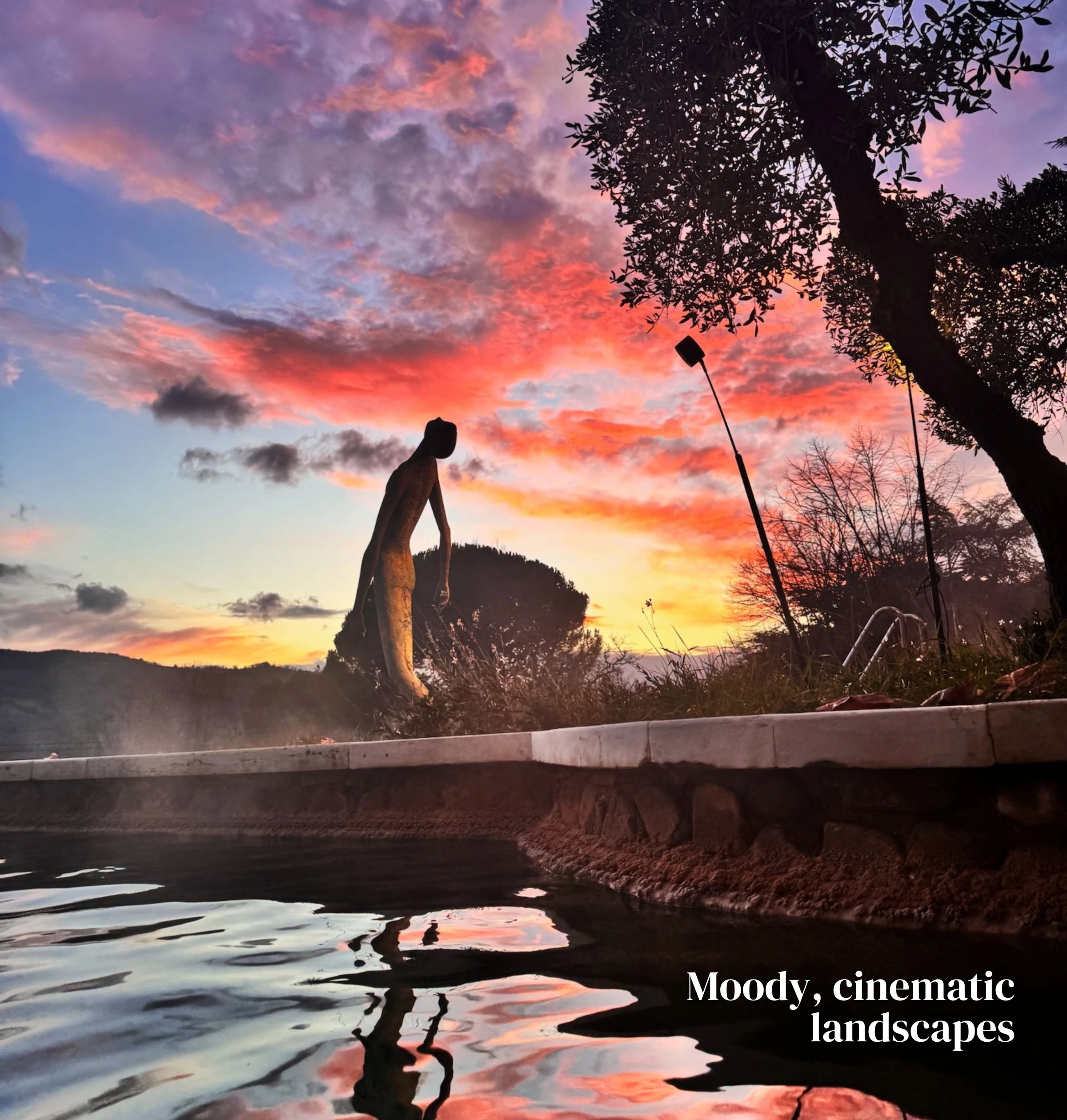 Thermal pool reflecting a vivid sunset beside a silhouetted garden sculpture