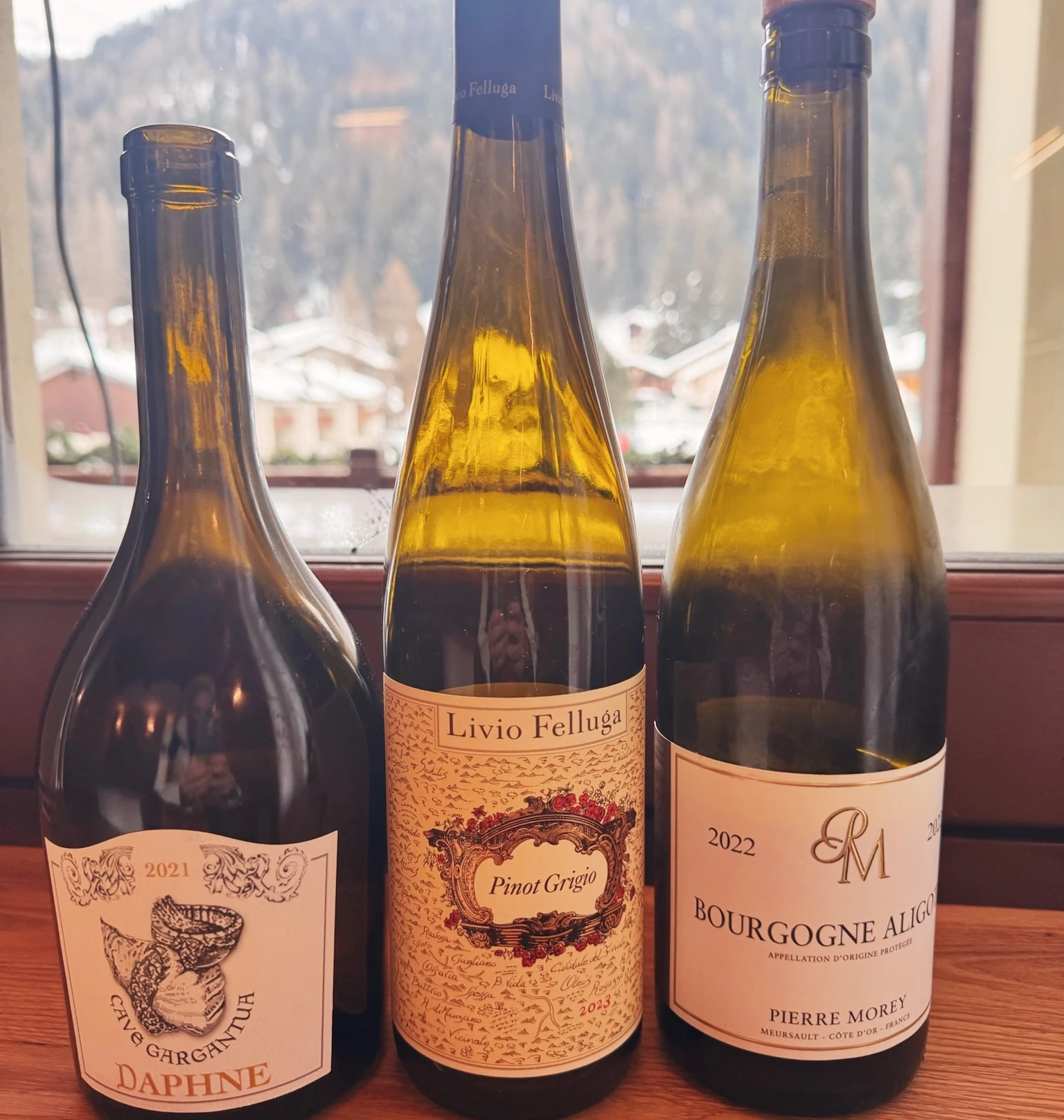 Three wine bottles, including Livio Felluga Pinot Grigio, stand before a snowy mountain view.