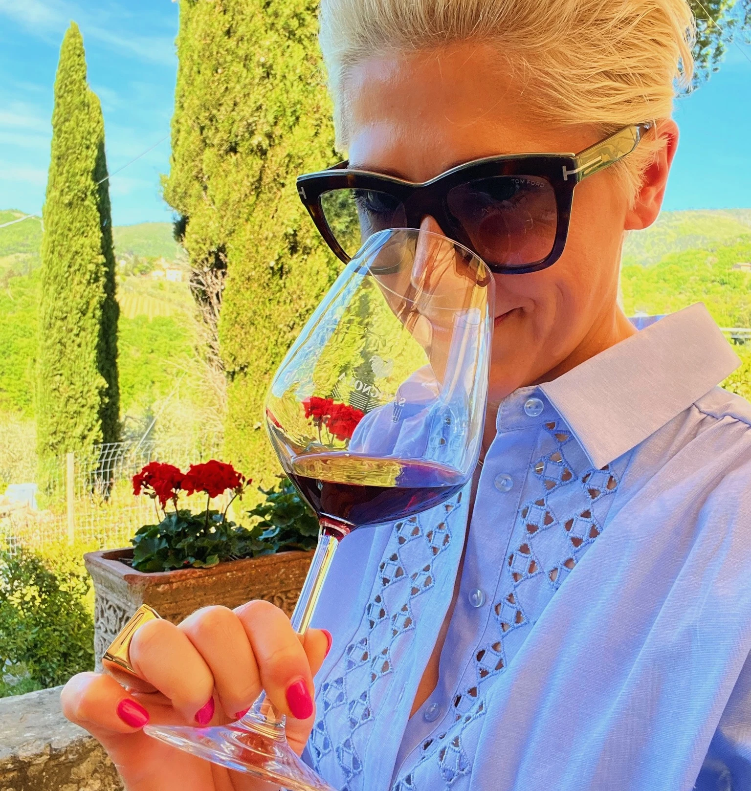 Elizabeth Hawthornthwaite smells red wine at Savignola, with Tuscan vineyards and cypress trees behind her