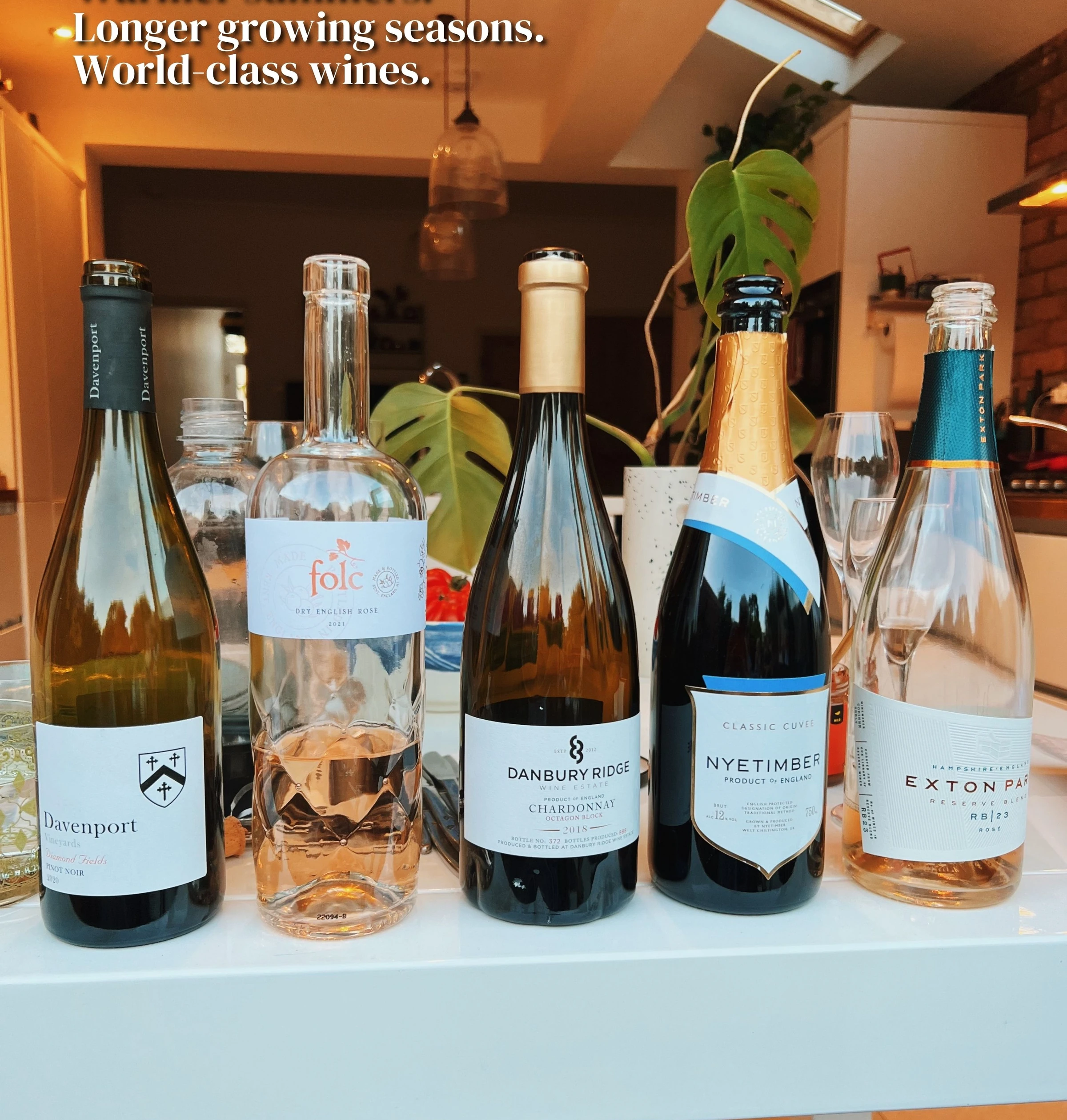 English wine bottles displayed on a table beneath text about warmer summers and longer growing seasons