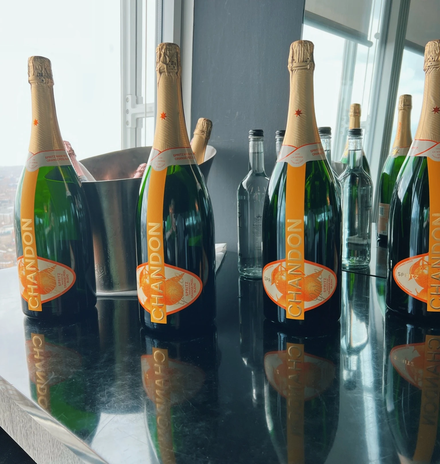Chandon bottles and clear spirit bottles arranged on a reflective table beside windows