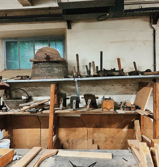 Traditional cooperage workshop with wooden barrels, hand tools and timber on shelves and a workbench