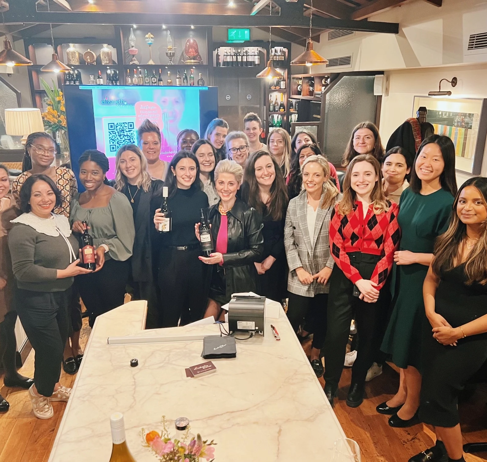 Group of women holding wine bottles and glasses at a bar for International Women's Day