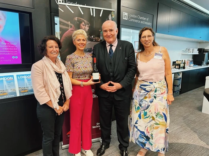 Four people pose at a London Chamber of Commerce event, with one holding a wine bottle