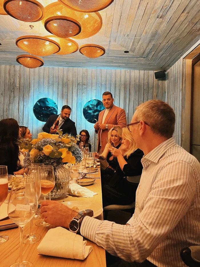 Guests enjoy a seated wine tasting as a presenter pours rosé at a restaurant table