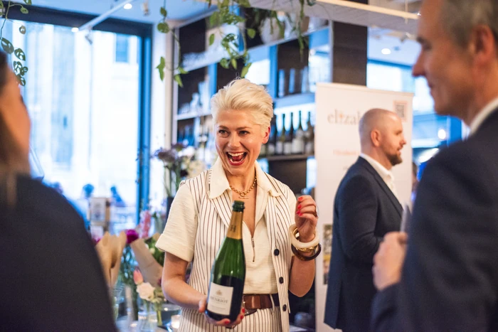 Woman holding a wine bottle while speaking to guests at an indoor tasting event