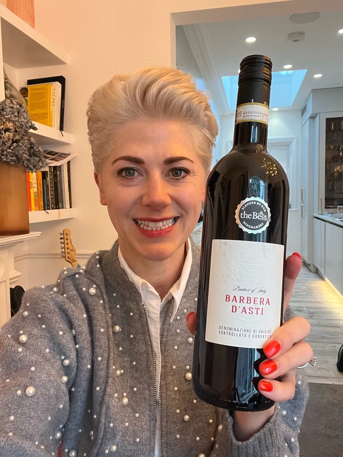 Smiling woman holding a bottle of Barbera d'Asti wine indoors