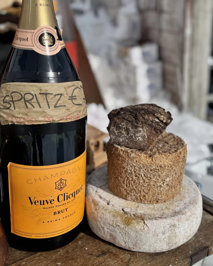 Veuve Clicquot Champagne beside a stack of three cheeses on a wooden table