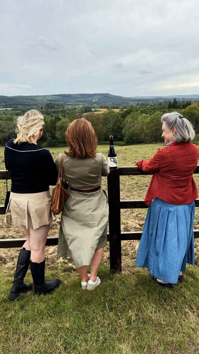 Three women look over a rolling English landscape beside a bottle of sparkling wine