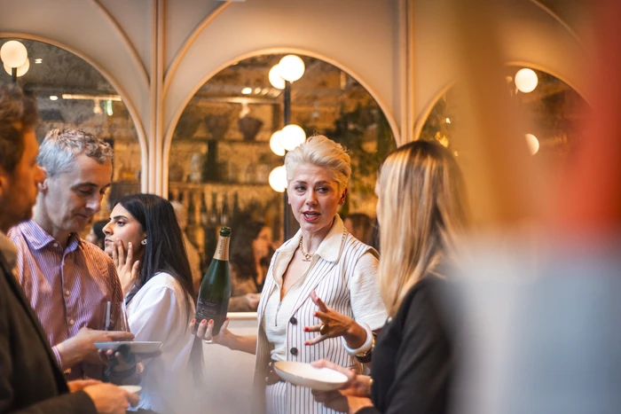 Guests gather around a woman holding a bottle of wine at an indoor tasting