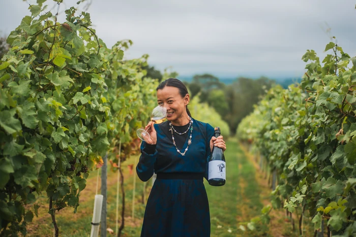 Woman holding a wine bottle and glass among vines at a vineyard