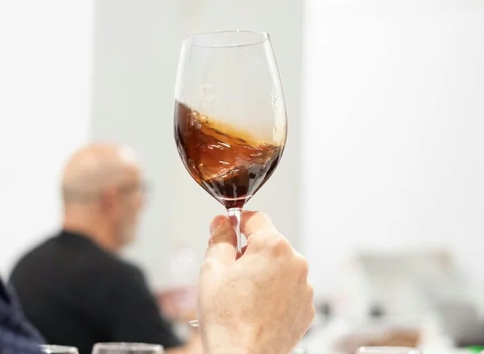 Hand holding a glass of amber wine at a tasting table