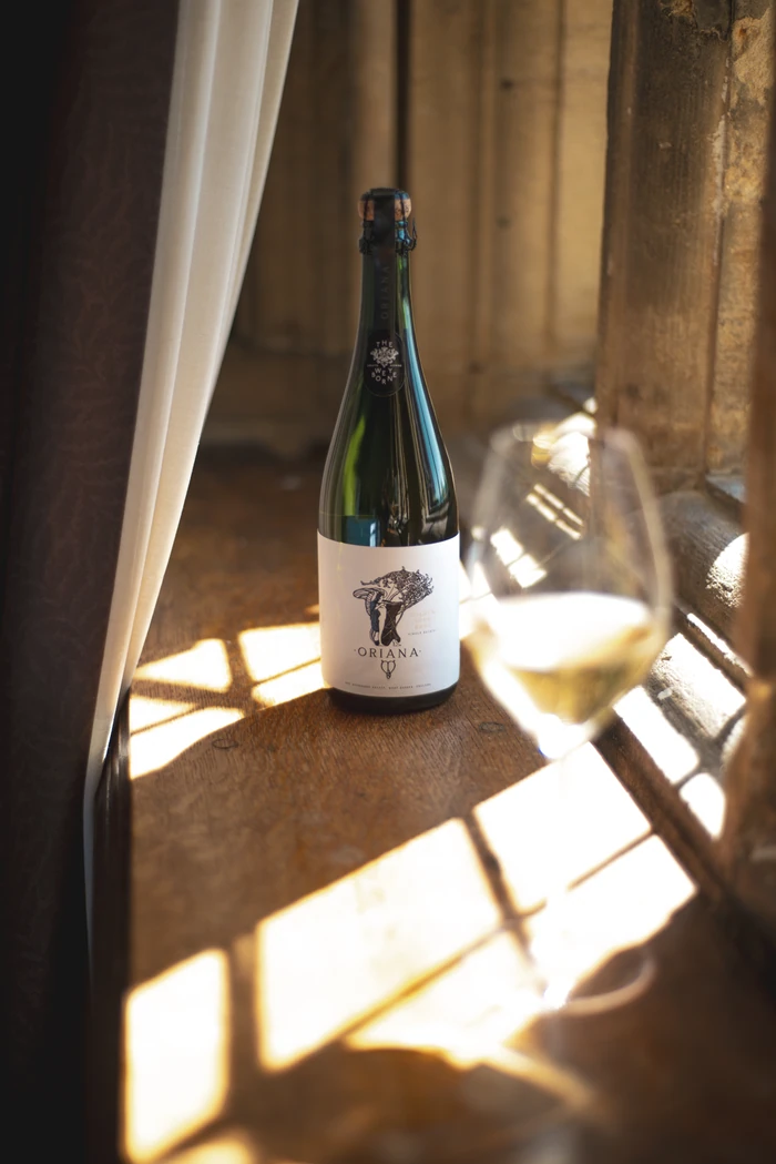 Oriana sparkling wine bottle beside a glass in sunlight