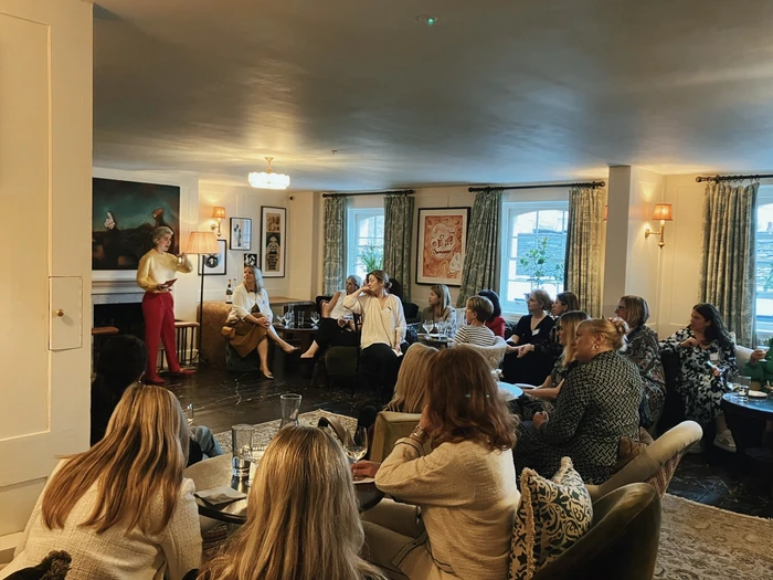 Women gathered for a wine tasting as a presenter speaks in an elegant lounge