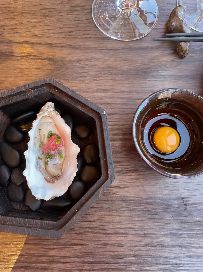 Oyster with garnishes, a raw egg yolk and wine glasses on a wooden table