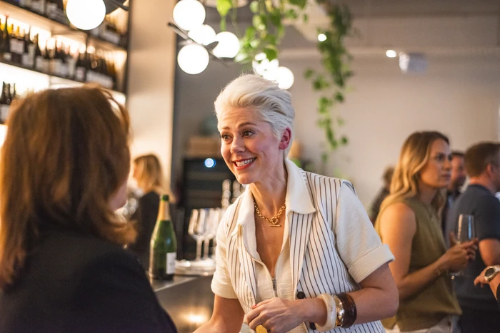 Wine host speaking with a guest at a lively indoor tasting event