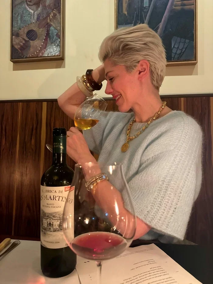 Woman tasting amber wine beside a bottle and two wine glasses in a restaurant