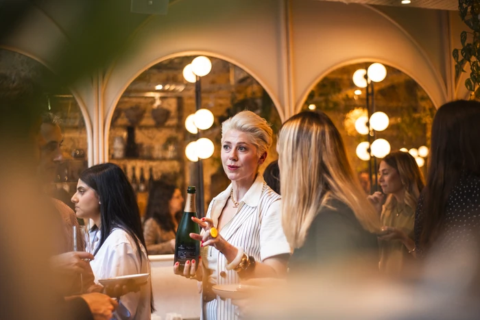 Guests gather indoors as a woman holds a wine bottle during a tasting