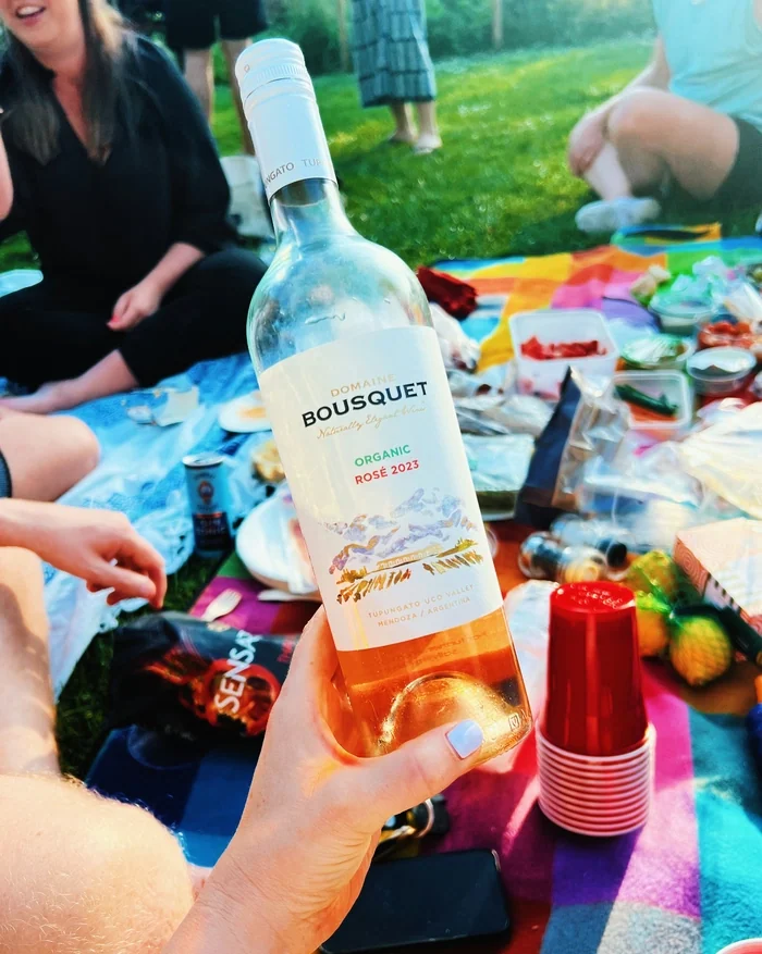 Bottle of Domaine Bousquet organic rosé held over a colourful picnic spread