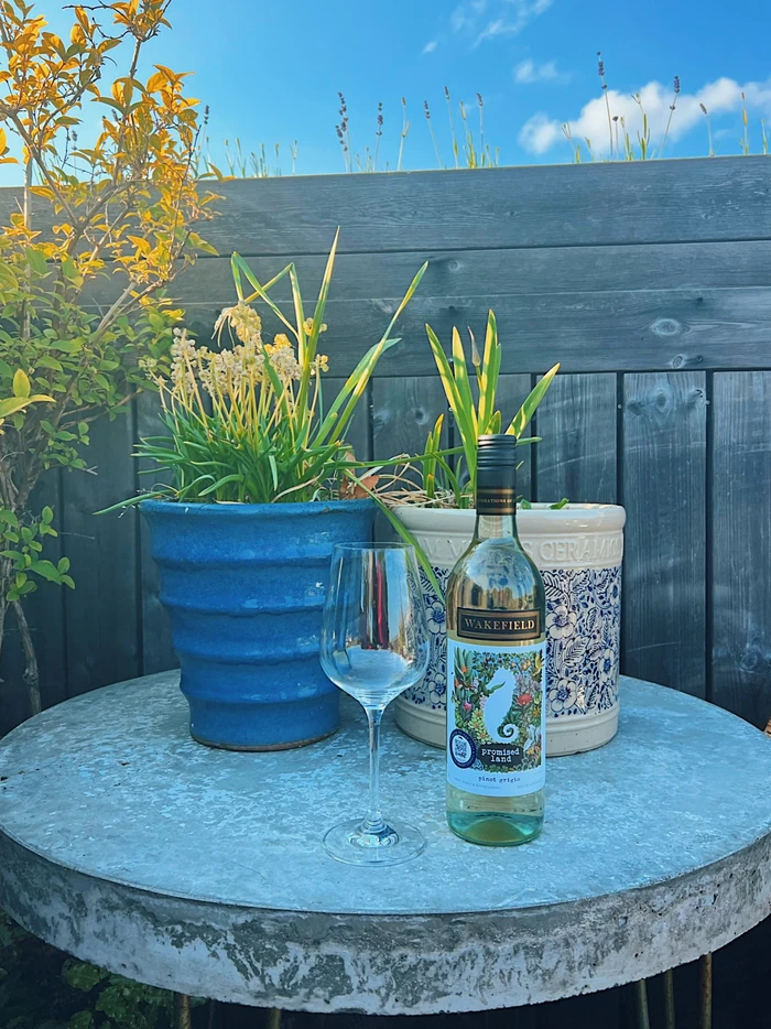 Wakefield Promised Land Pinot Grigio beside a wine glass on a garden table