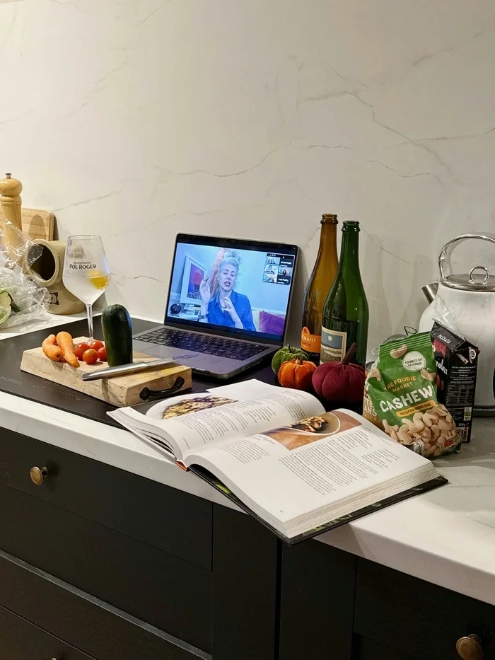 Virtual wine tasting setup with wine, snacks, vegetables and a presenter on a laptop