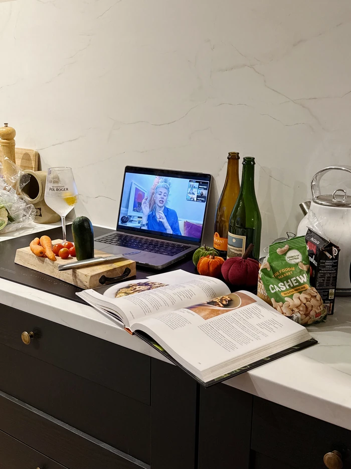 Virtual wine tasting setup with wine, snacks, vegetables and a presenter on a laptop