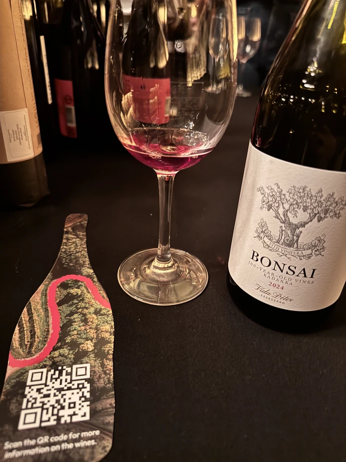Glass of red wine beside a Bonsai 2024 wine bottle and tasting card