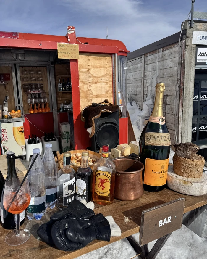 Outdoor mountain bar serving cocktails, sparkling wine, spirits and cheese beside a snowy ski area