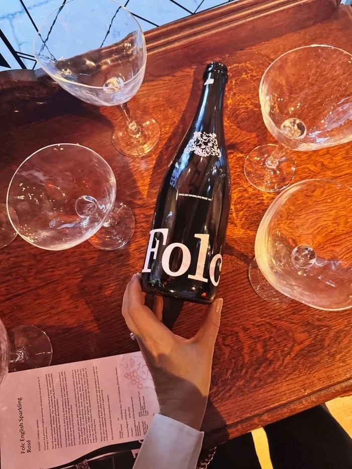 Foll English sparkling rosé bottle held above a wooden tasting table with glasses and tasting notes