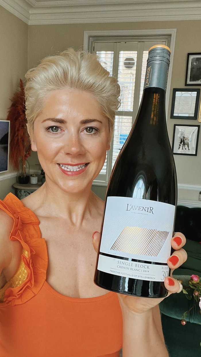 Smiling woman in an orange top holding a large bottle of L'Avenir Chenin Blanc