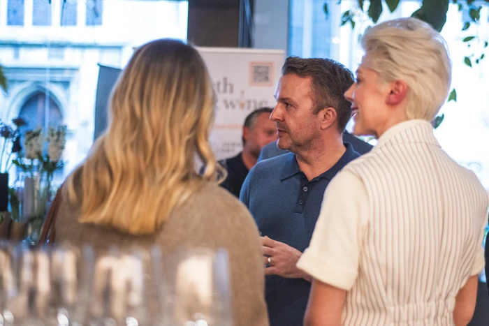 Guests chat at a wine event in a bright venue, with blurred wine glasses in the foreground
