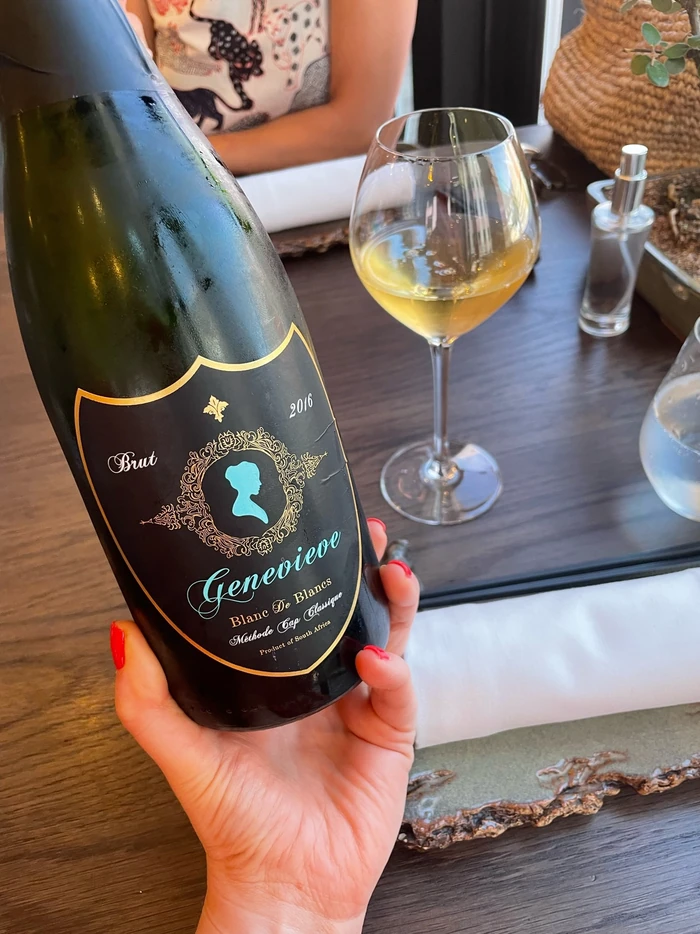 Bottle of Genevieve Brut sparkling wine beside a glass of poured wine at a dining table