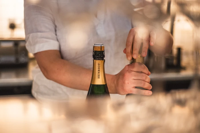 Person in a white shirt opens a bottle of Henriot Champagne
