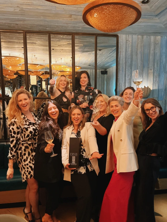 Group of women raising wine glasses in a restaurant, with a Porte Noire bottle