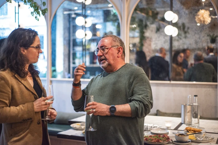 Guests chat over wine at a tasting event with food and wine glasses on the table