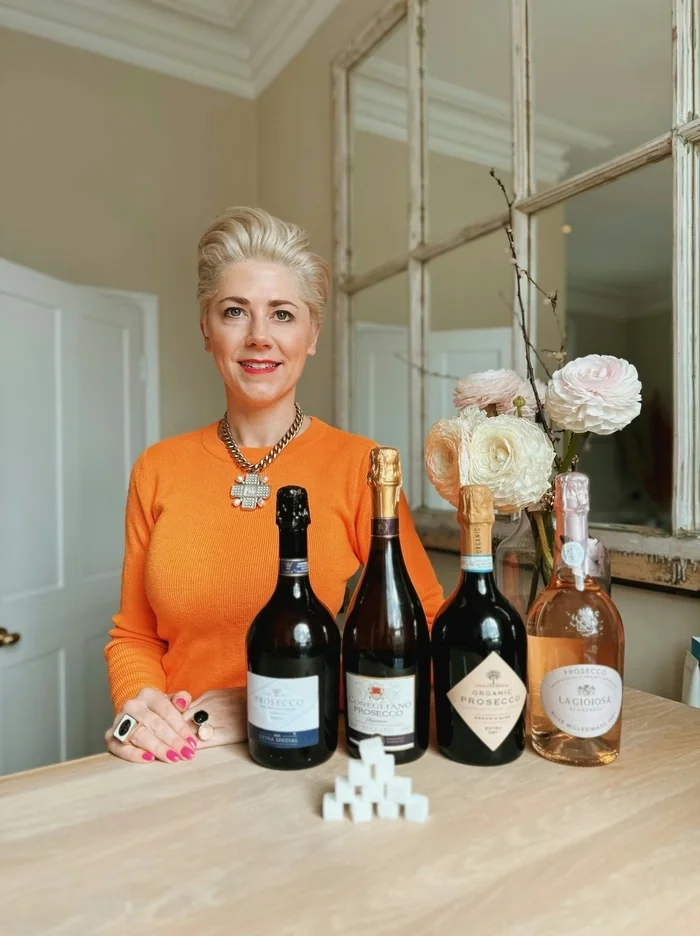 Woman in an orange top standing behind four bottles of Prosecco and sugar cubes