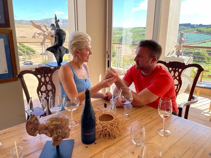 Two people tasting wine at a table overlooking vineyards and hills